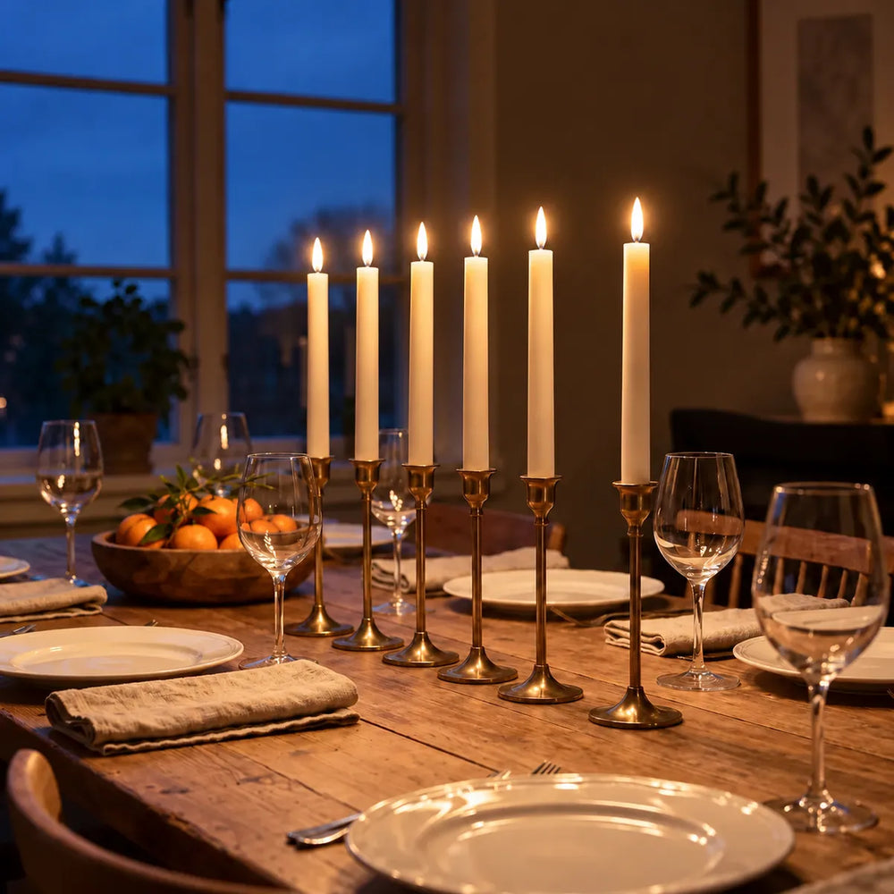 Six bougies flambeaux LED Wove Luma allumées dans des bougeoirs en laiton sur une table dressée un soir d'hiver