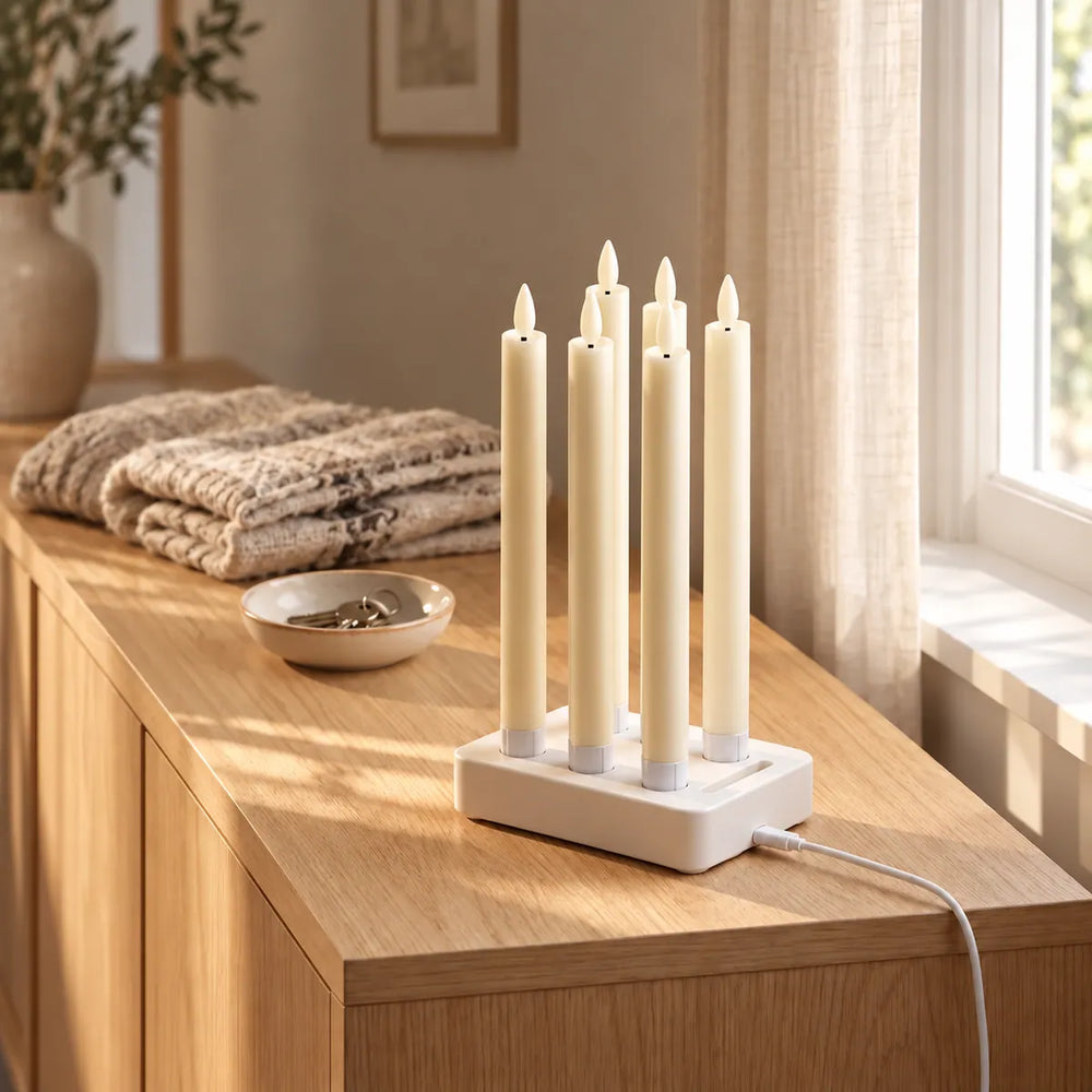Six bougies flambeaux LED Wove Luma en charge sur le socle blanc posé sur une commode en chêne au soleil du matin