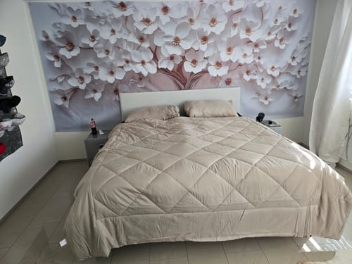 Couette Wove couleur sable sur un grand lit dans une chambre d'amis au papier peint fleuri