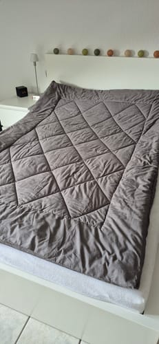 Couette Wove gris-beige repliée sur un lit blanc avec une guirlande lumineuse au-dessus