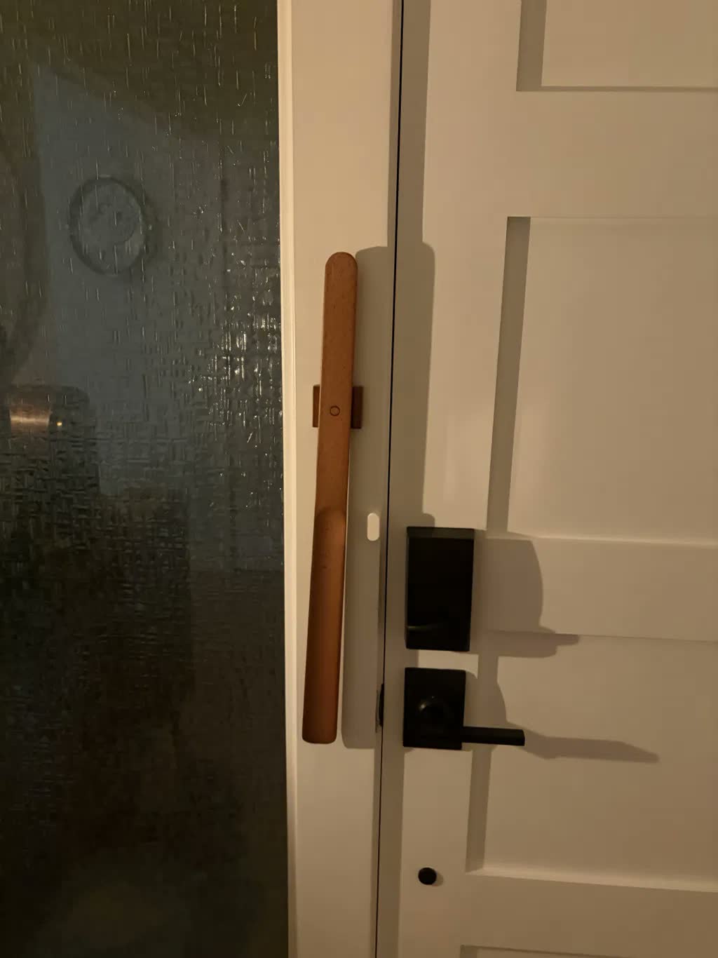Chausse-pied en hêtre clair fixé par aimant sur un encadrement de porte blanc, à côté d'une poignée noire et d'une serrure connectée