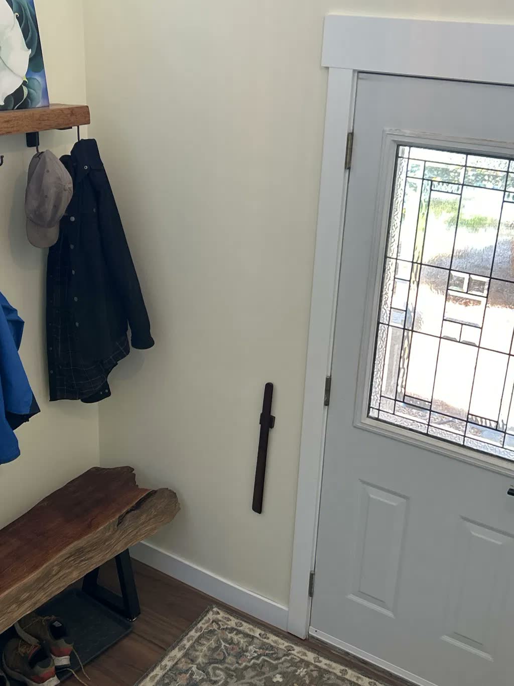 Chausse-pied en noyer foncé sur un mur d'entrée crème, avec un banc en bois brut, des patères et une porte d'entrée vitrée à petits carreaux