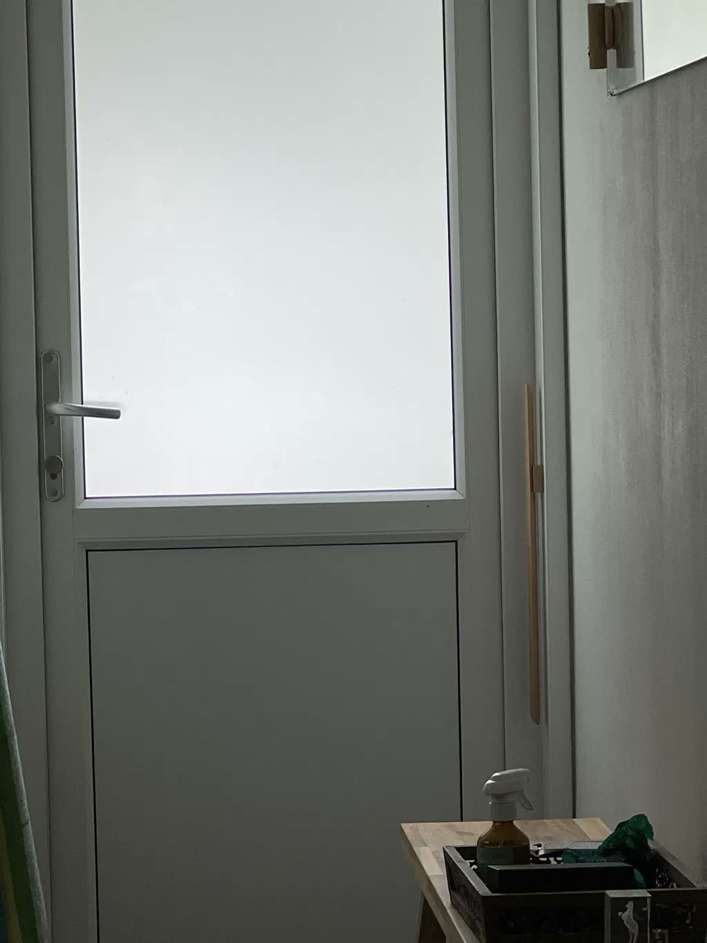 Chausse-pied en hêtre naturel sur un mur grège à côté d'une porte de jardin blanche au verre dépoli