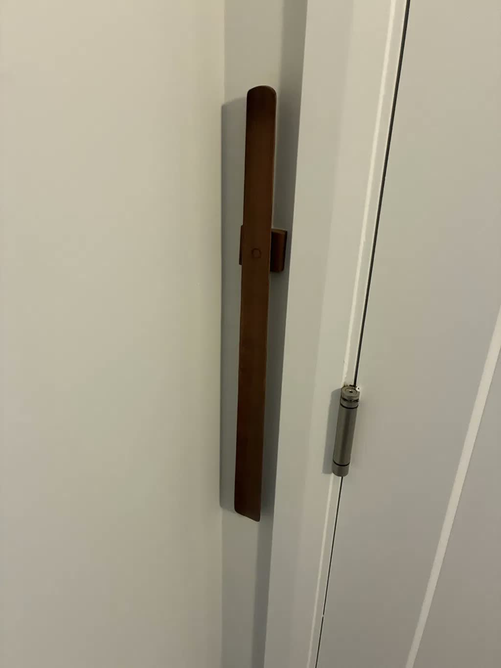 Gros plan d'un chausse-pied en noyer foncé sur un mur blanc à côté d'une porte blanche dont on voit la charnière