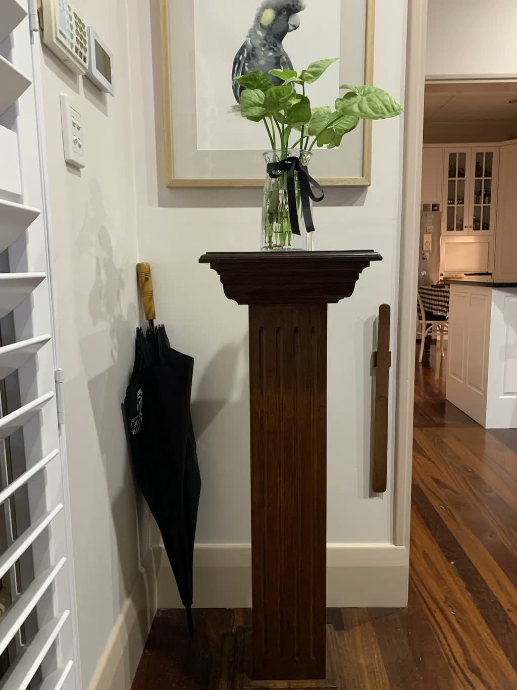 Chausse-pied en noyer foncé sur un mur d'entrée blanc à côté d'un guéridon ancien en bois sombre, avec un vase en verre et un parapluie noir